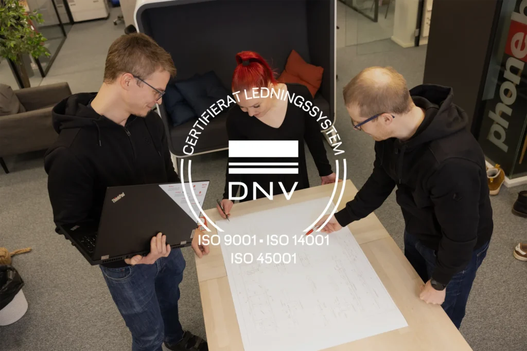 Tre Anfra-medarbetare granskar ritningar och planerar tillsammans på kontoret. Över bilden visas DNV:s märke för certifierat KMA-ledningssystem enligt ISO 9001, ISO 14001 och ISO 45001.
