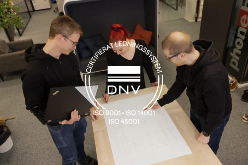 Tre Anfra-medarbetare granskar ritningar och planerar tillsammans på kontoret. Över bilden visas DNV:s märke för certifierat KMA-ledningssystem enligt ISO 9001, ISO 14001 och ISO 45001.