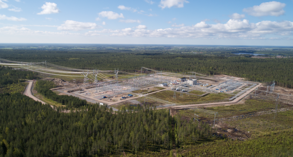 Flygbild över ett transformatorstationsområde, omgivet av skog. På området syns kraftledningar, stålkonstruktioner och byggvägar.